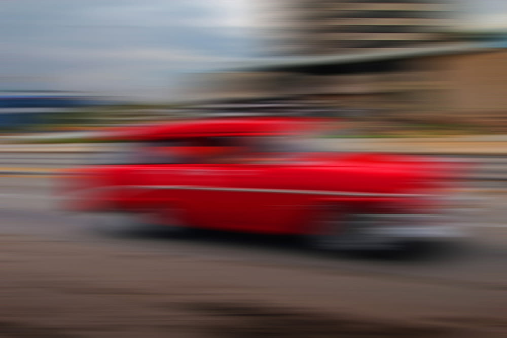 Un'auto rossa che guida lungo una strada accanto a un edificio alto