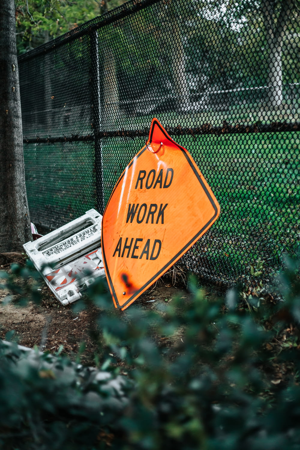 road work ahead signage leaning on chain link fence