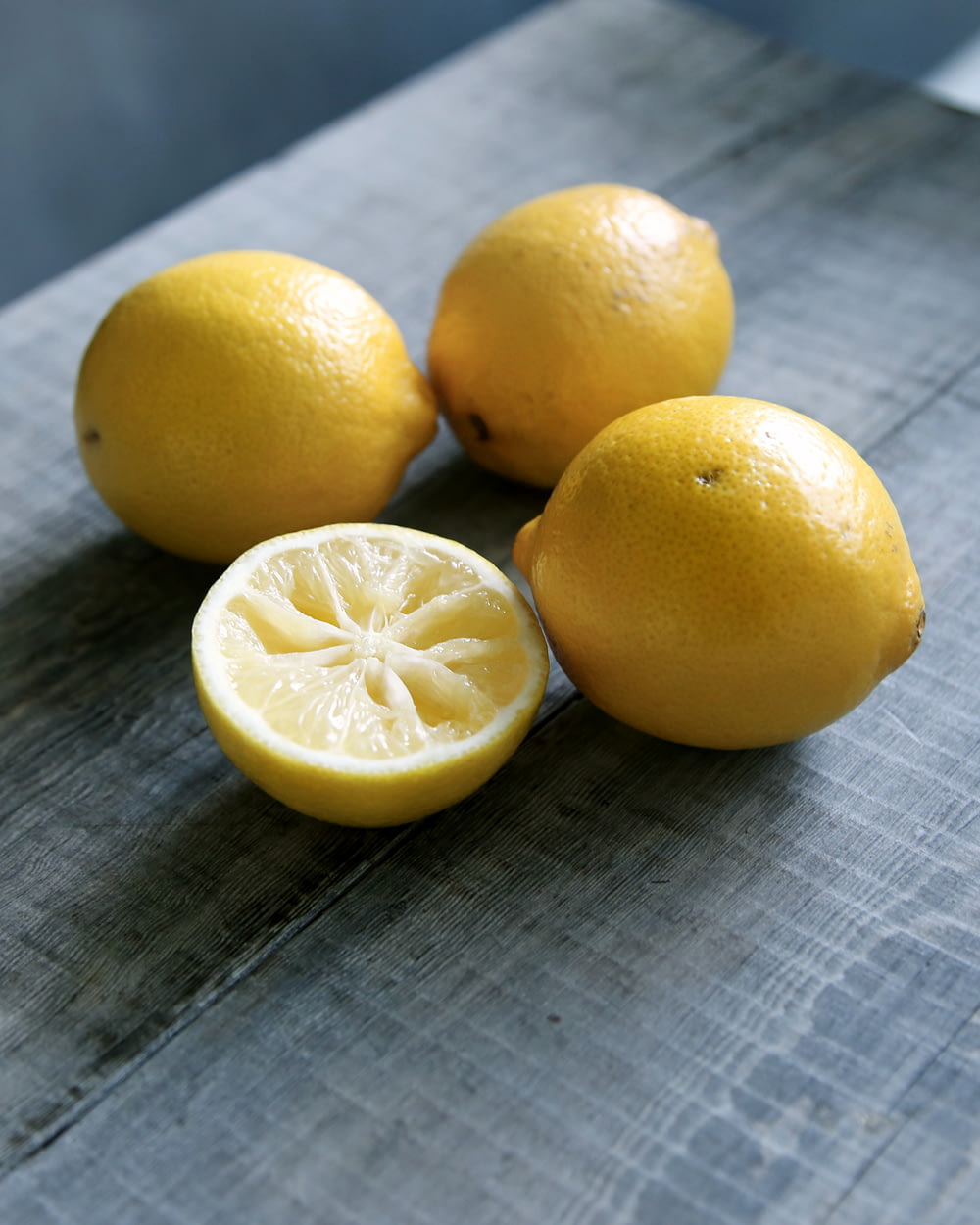 trois citrons jaunes à côté d’un citron tranché placé sur une surface en bois gris