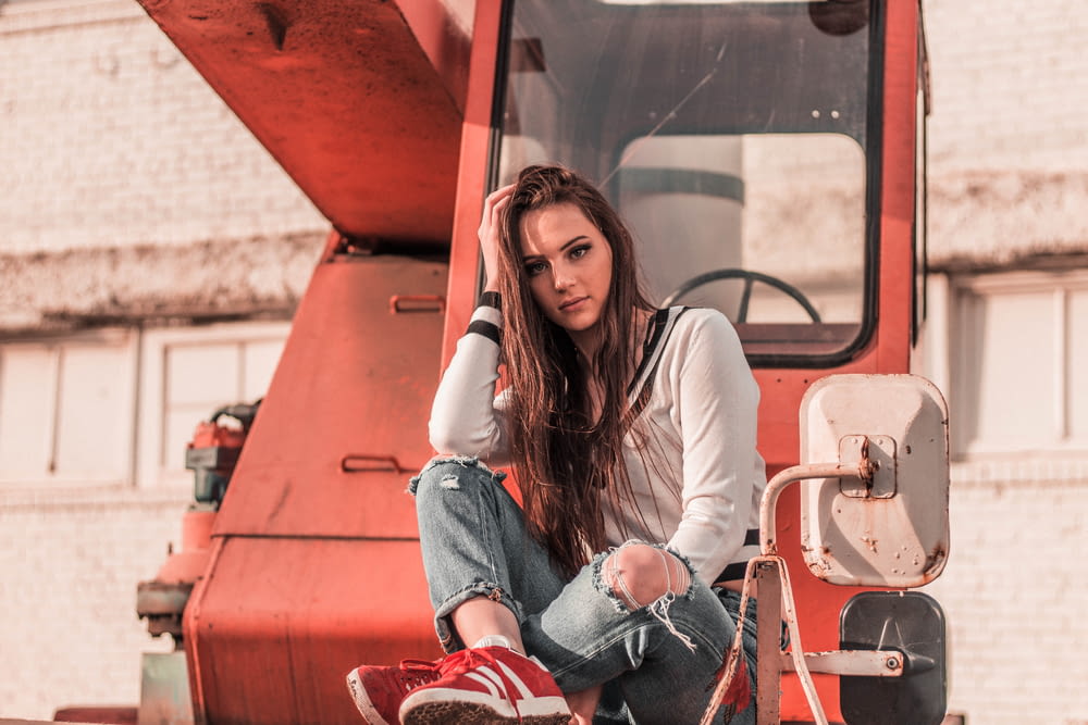 woman sitting in front of red heavy equipment while resting her hand on head