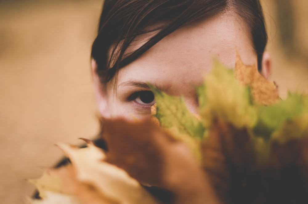 Foto de enfoque selectivo de mujer escondida en planta de hojas verdes y marrones
