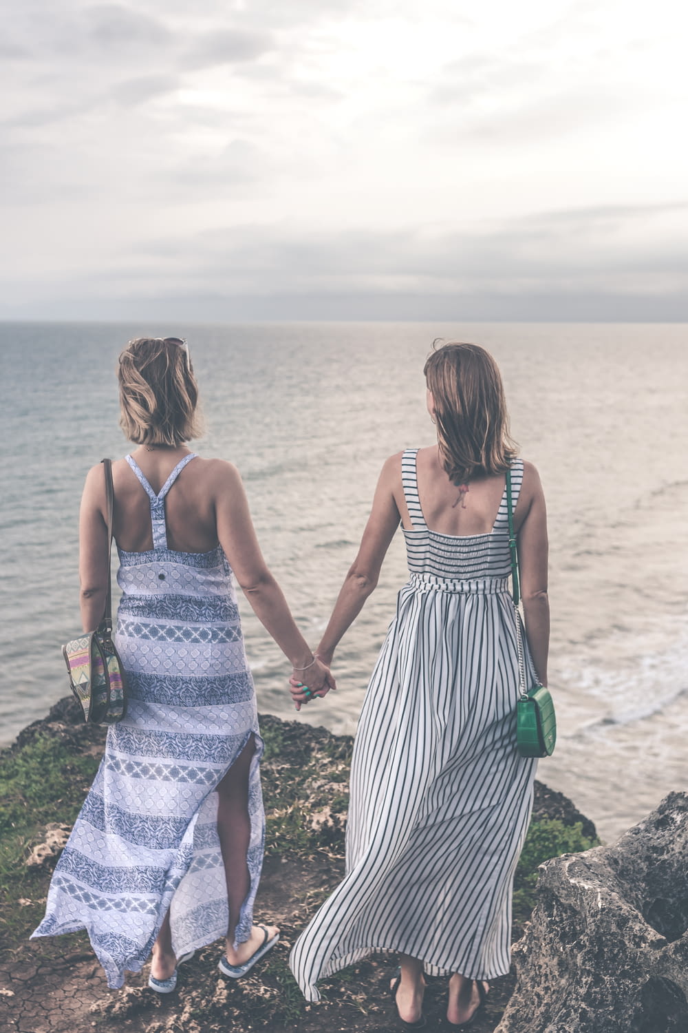 two woman in maxi dresses holding each other hand while standing on cliff