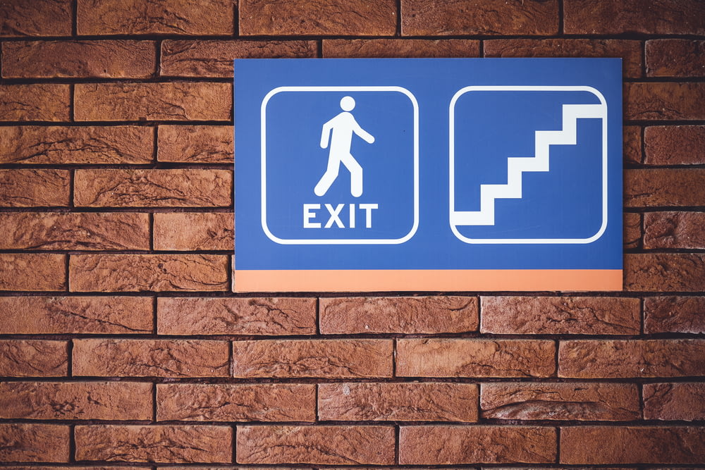blue and white exit signage mounted on brown brick wall