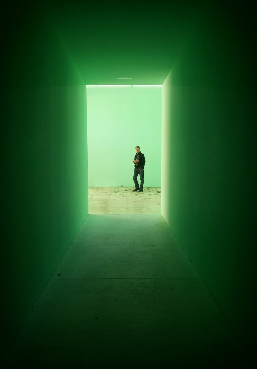 man in black jacket stands near green wall