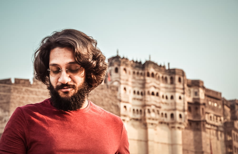 man wearing red crew-neck shirt standing near the ancient palace
