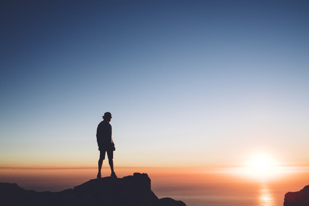 Silhouettenfoto eines Mannes, der auf dem Gipfel vor dem Meer steht