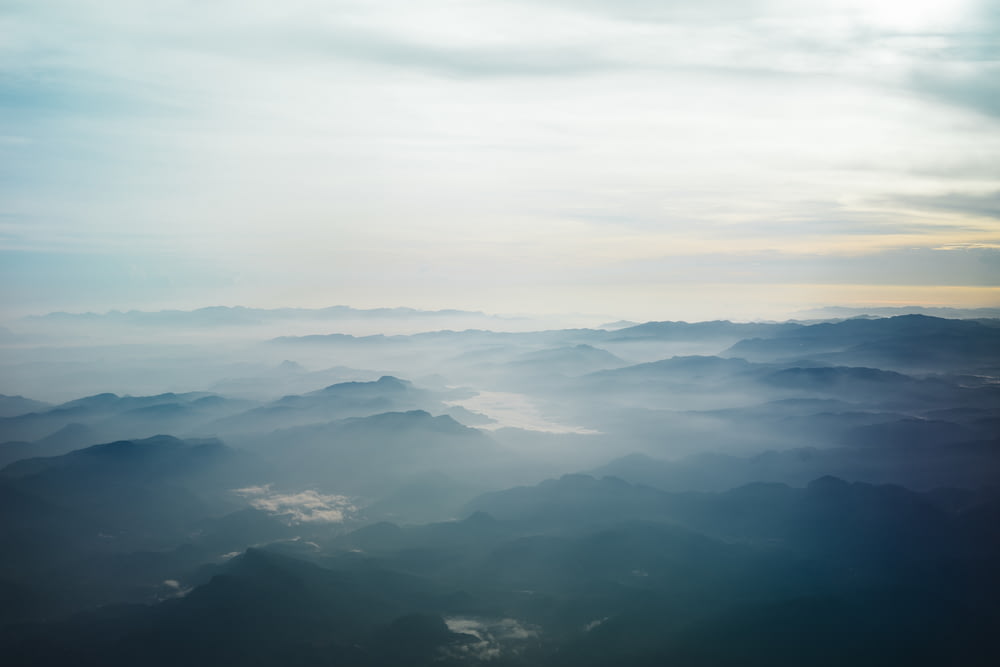 aerial photography of blue mountains surrounded by fogs under white sky at daytime