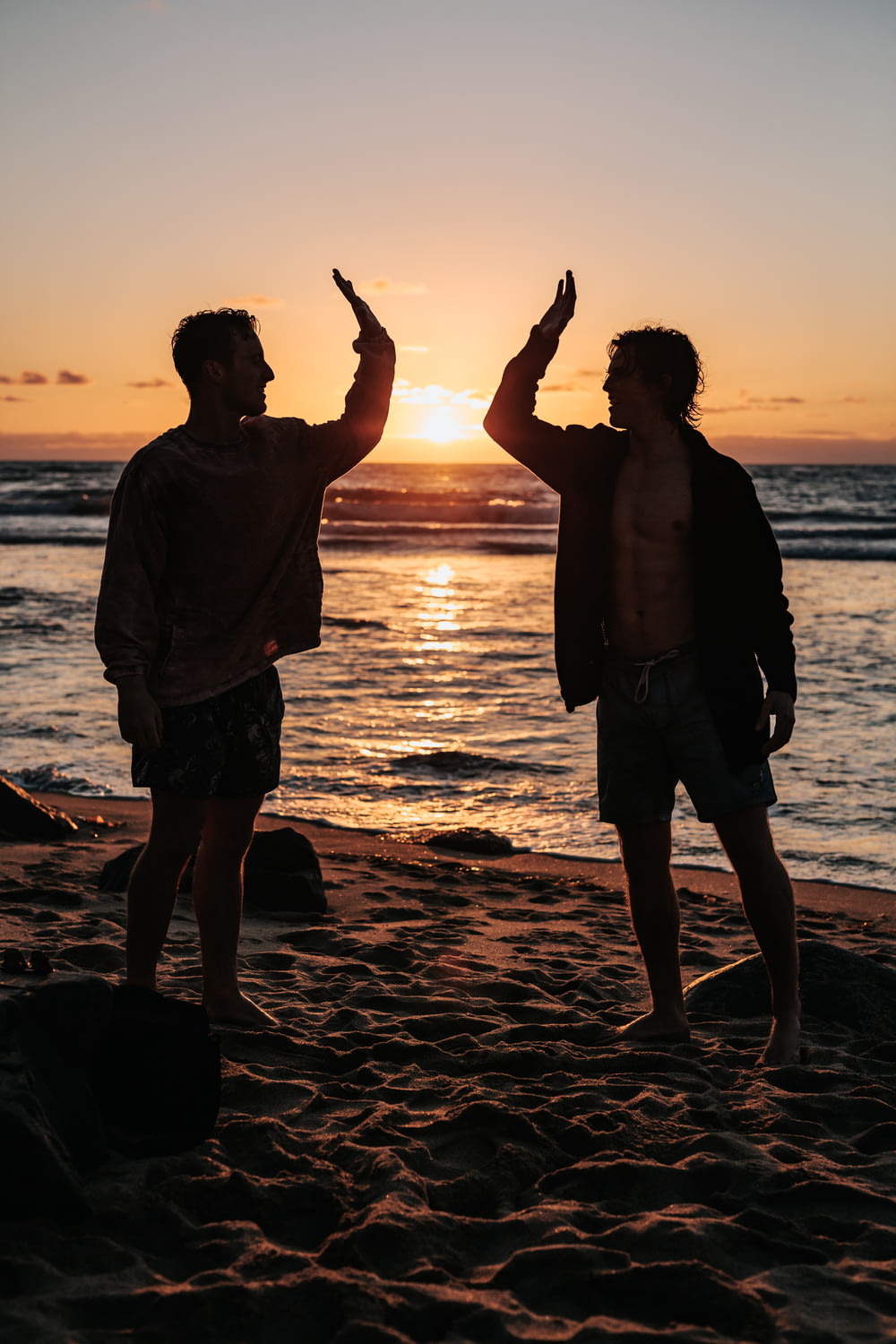 silhouette di due uomini vicino alla riva del mare in procinto di battere il cinque durante il tramonto