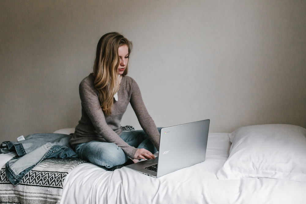 donna che digita su MacBook Pro mentre è seduta sul letto in camera