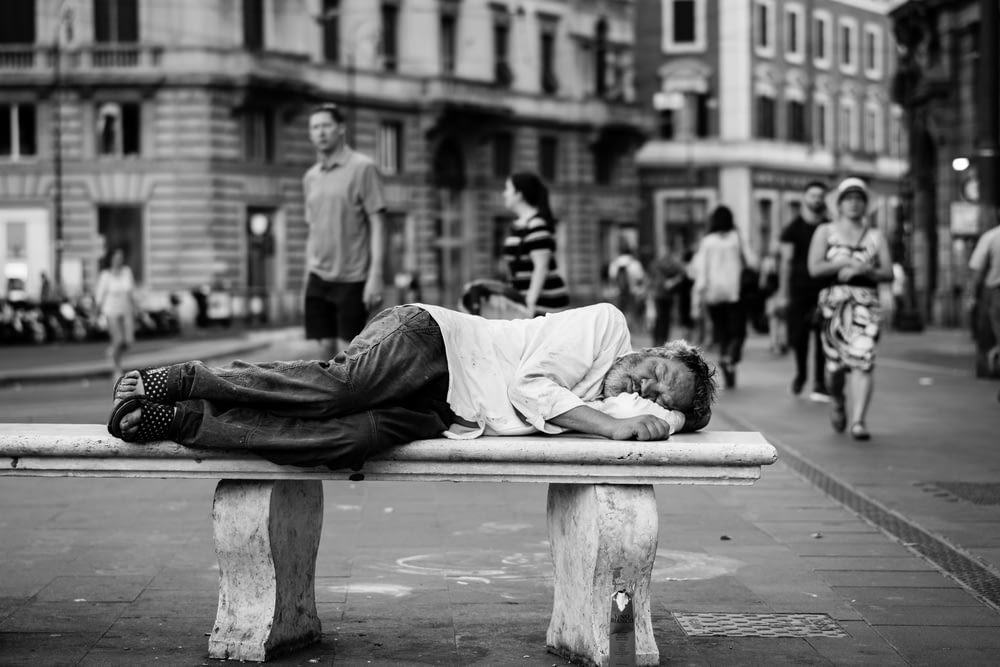 homem dormindo no banco no meio da rua