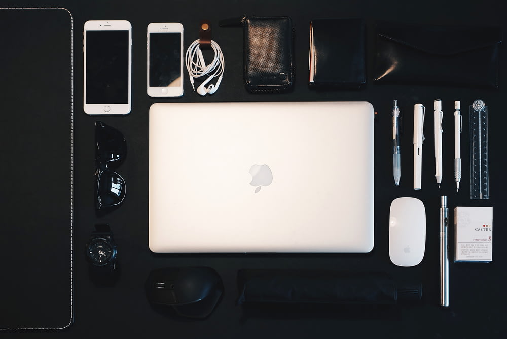MacBook prateado entre Magic Mouse, lápis, óculos de sol e iPhone
