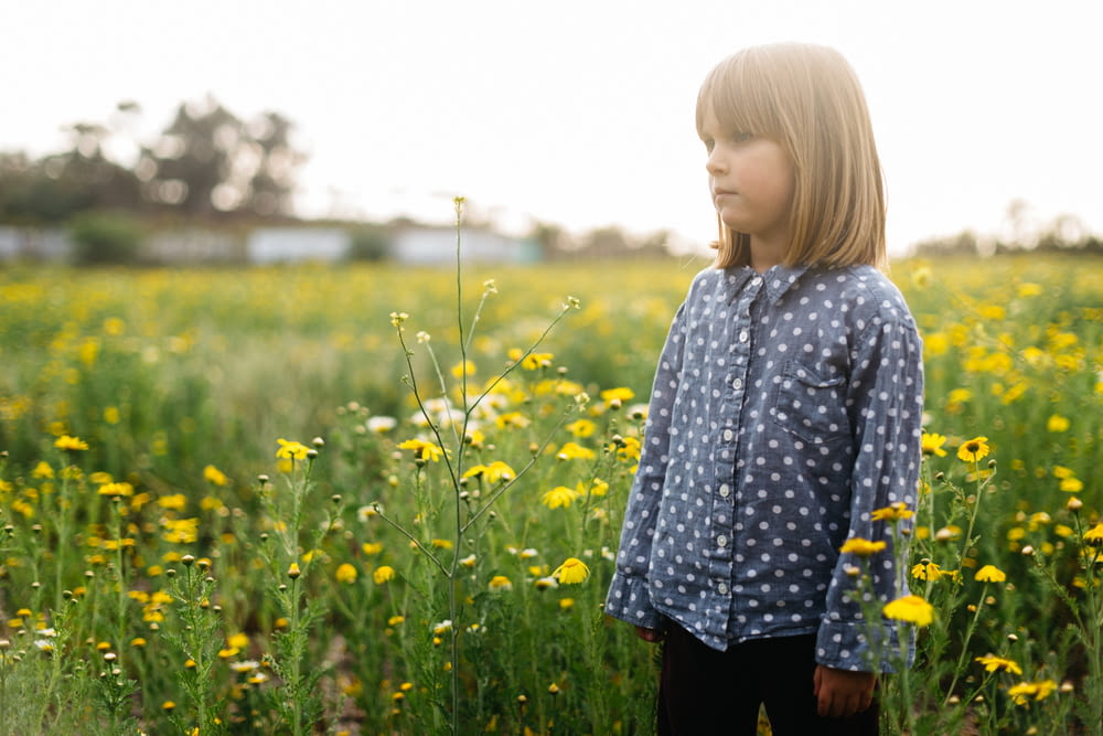girl standing surrounded by yellow flowers during daytime