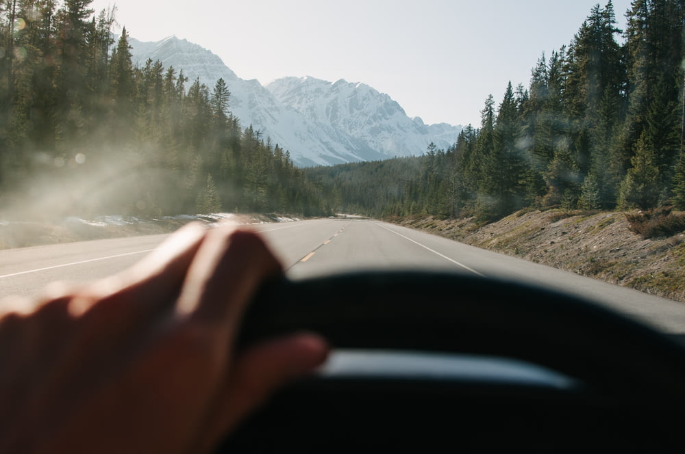 Una persona che guida un'auto su una strada con le montagne sullo sfondo