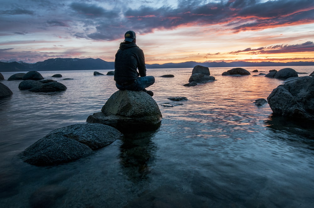 uomo seduto sulla roccia circondato dall'acqua