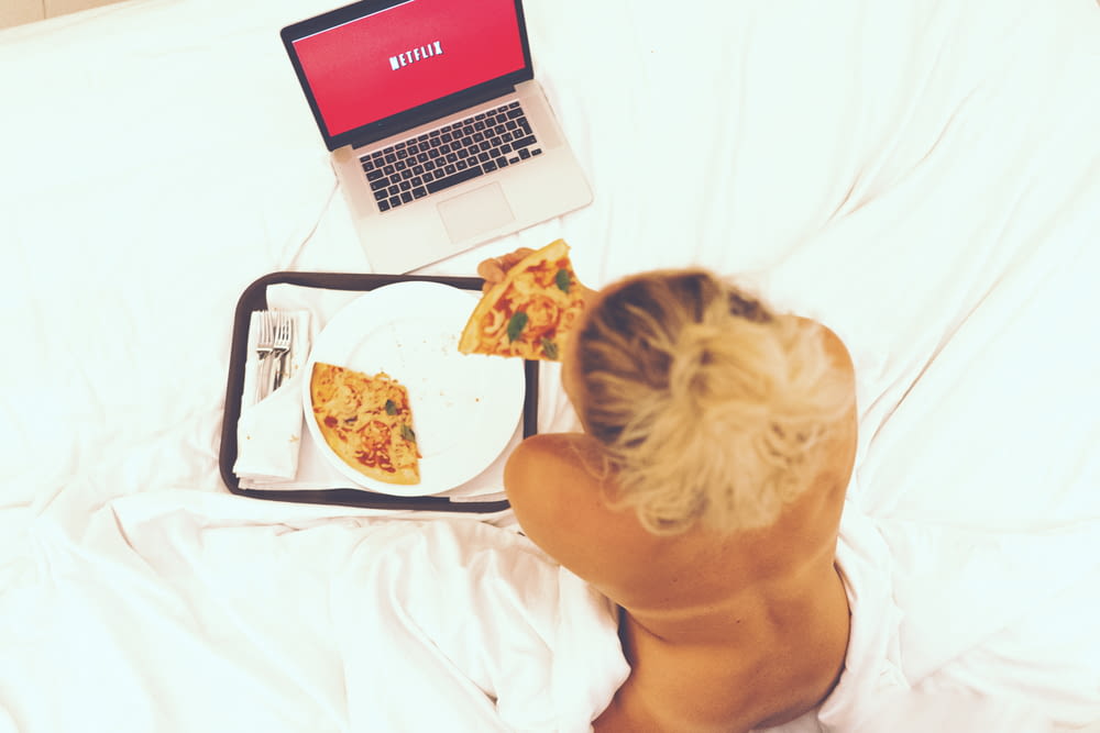 Frau sitzt auf dem Bett, während sie Pizza isst