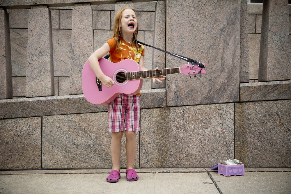 menina que toca guitarra perto da parede