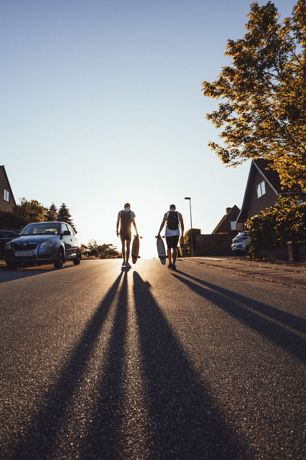 two men walking on road while holding longboard
