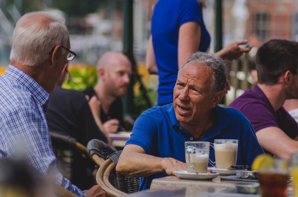 Hombre en polo azul hablando con un hombre mientras bebe café