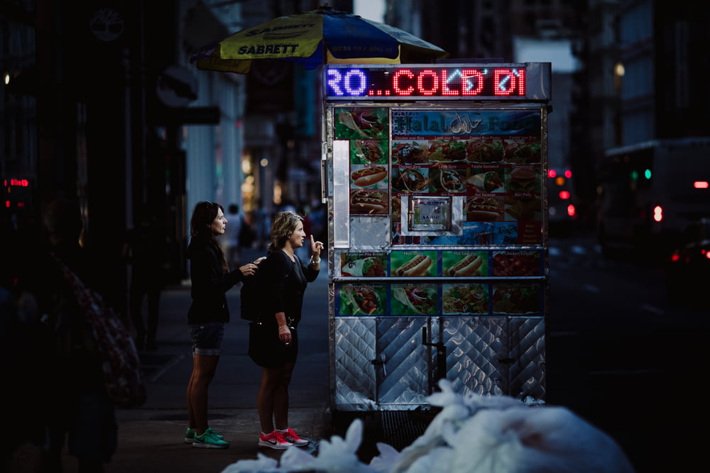 two woman buying food on gray food stall at nighttime