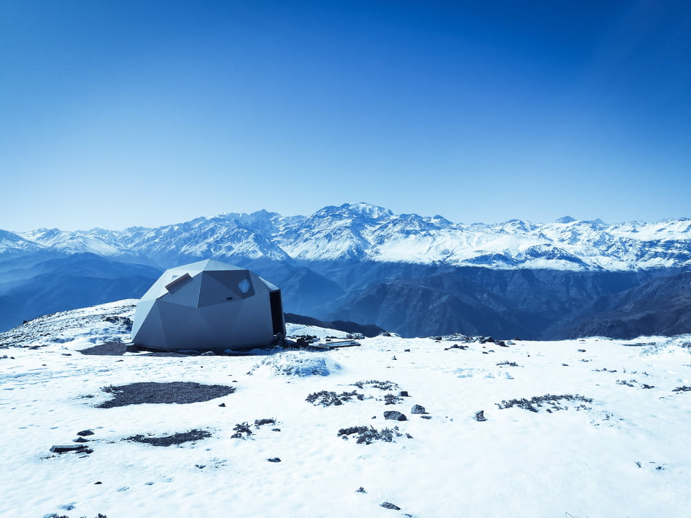 Graues Kuppelzelt auf Schneeoberfläche mit Blick auf schneebedeckte Berge unter blauem Himmel bei Tag