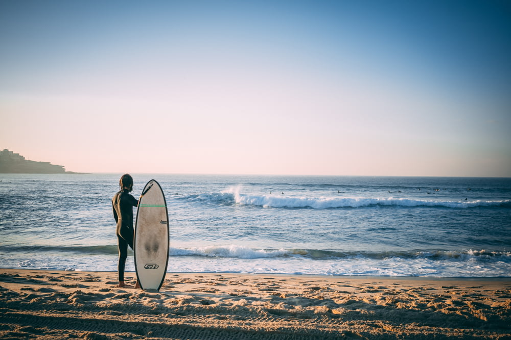 Persona nuda che tiene la tavola da surf sulla riva della spiaggia