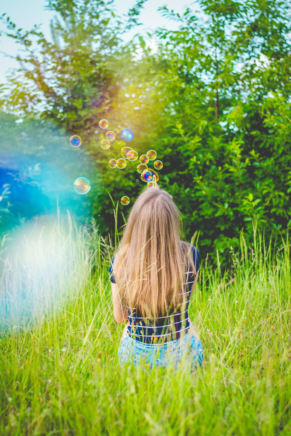 Ragazza che si siede mentre gioca a bolle sul campo di erba verde vicino agli alberi a foglia verde durante il giorno