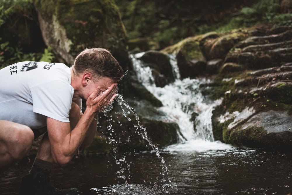 man wash his face at the body of water during daytime