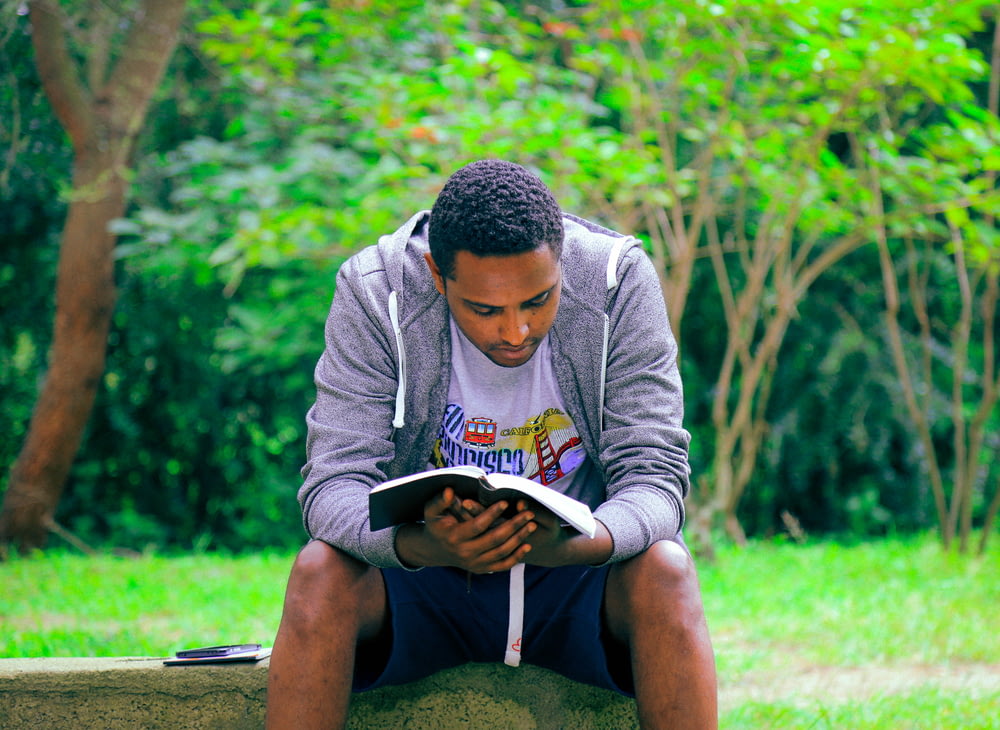 uomo seduto su una panchina di cemento che legge il libro