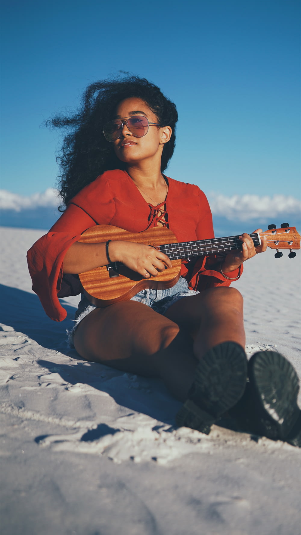woman playing ukalele while sitting on gray sand