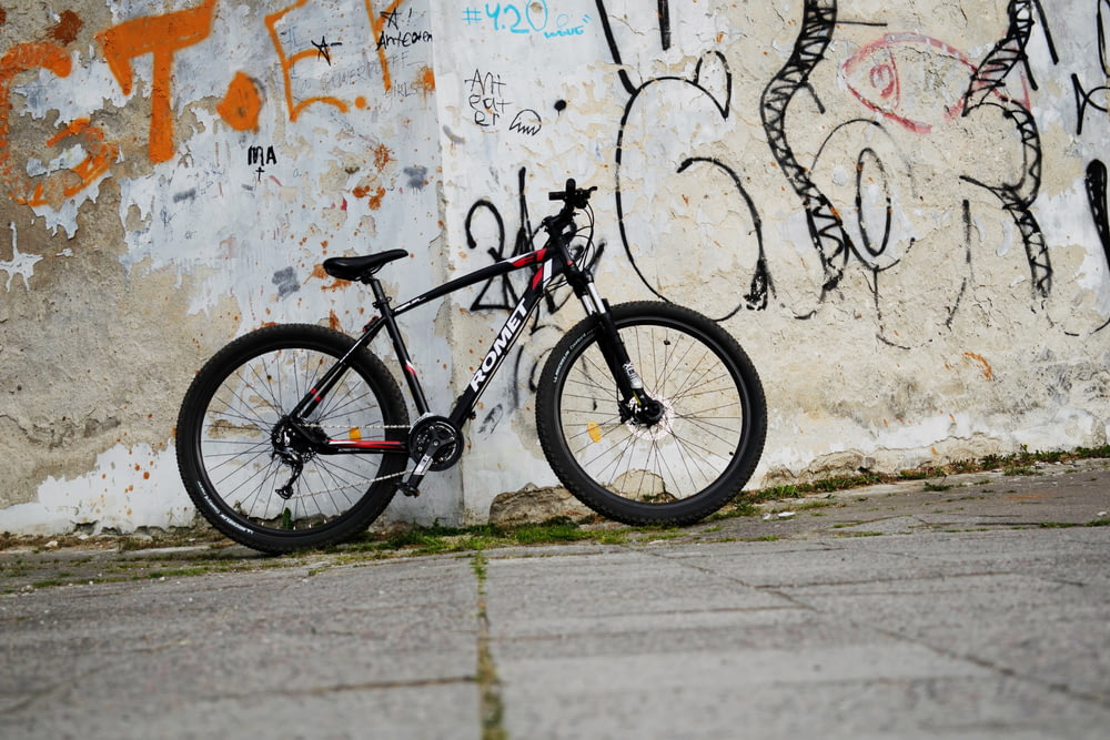 Bicicleta rígida negra apoyada en una pared de hormigón blanco