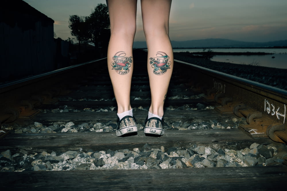 person standing on railroad with foot tattoo