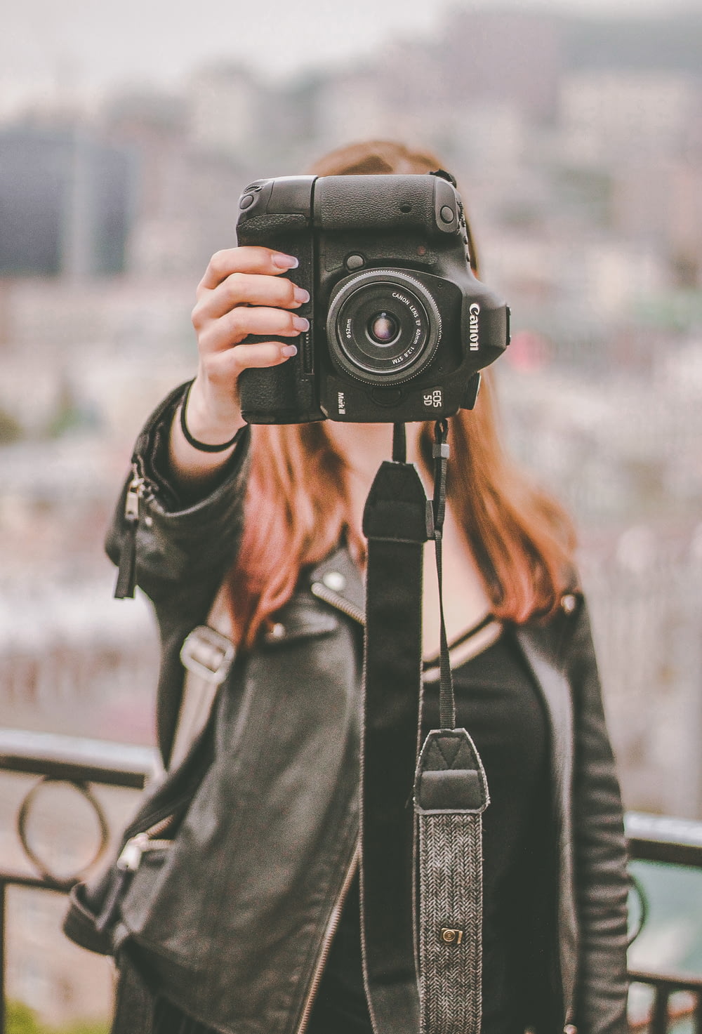 woman in black leather jacket holding black Canon DSLR camera