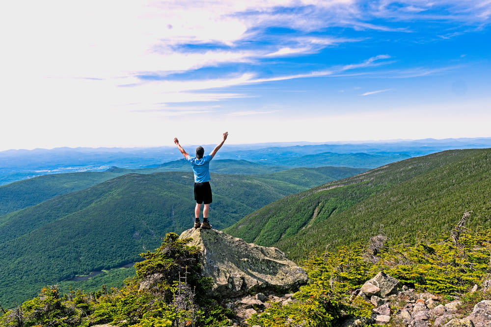 man raising his hands standing on mountain range