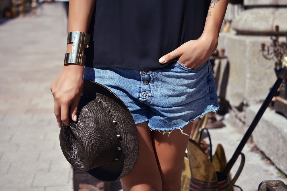 person wearing blue denim short shorts and holding black trilby hat