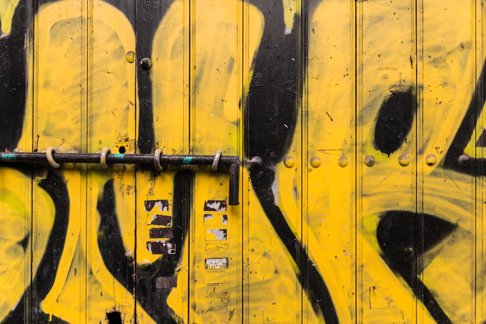 yellow and black wooden gate with graffiti and metal pole