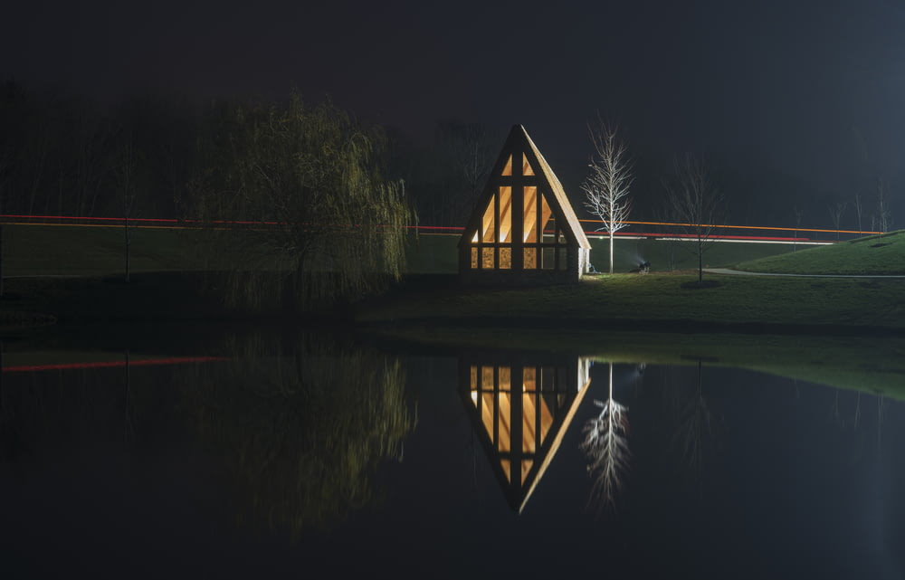 brown wooden house near bare tree with reflection on water at night time