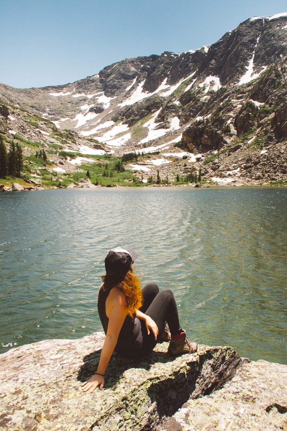 Femme assise sur une formation rocheuse regardant à travers la montagne Snowcap près du plan d’eau