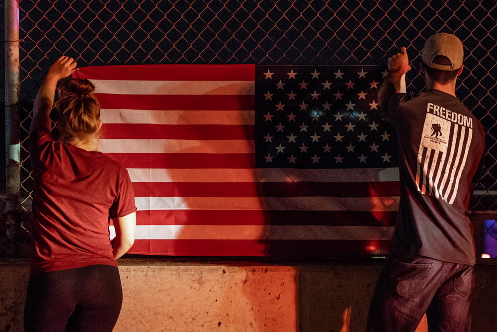 woman and man holding U.S.A. flag near gray wire fence