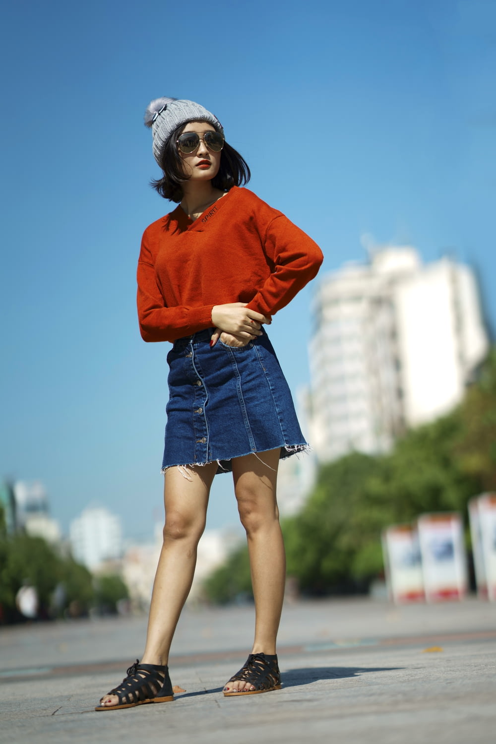 selective focus of woman wearing red long-sleeved shirt and blue denim skirt standing on road