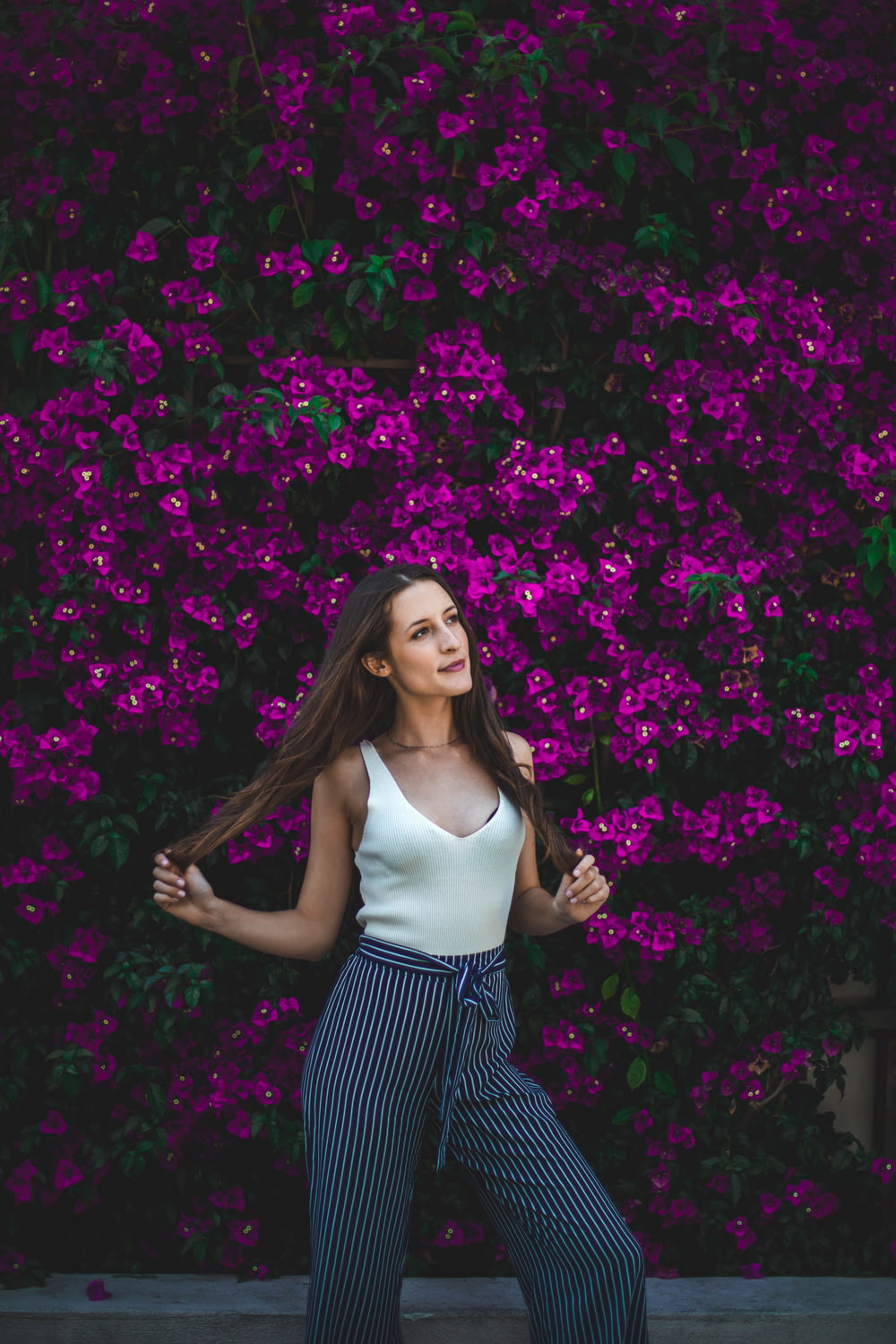 smiling woman holding her hair in front of purple flowers during daytime