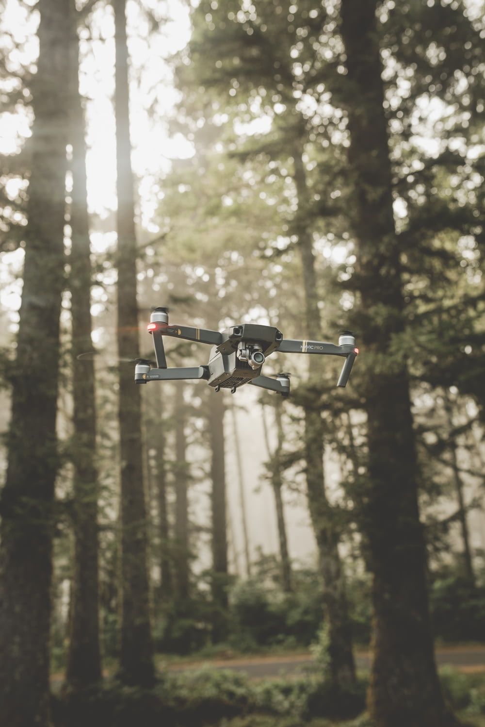 graue und schwarze DJI Mavic Pro Quadrocopter-Drohne auf mittlerer Höhe in der Nähe eines Waldes am Tag