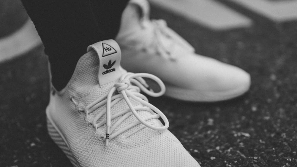 grayscale photo of person in white adidas low-top sneakers