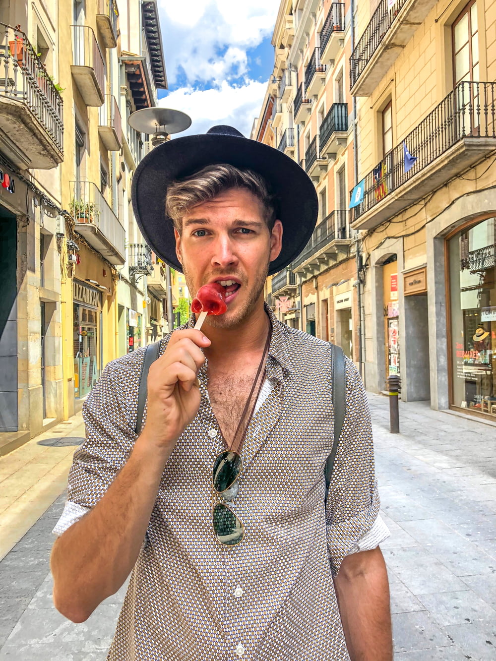 man wearing hat and grey shirt biting red candy on a stick