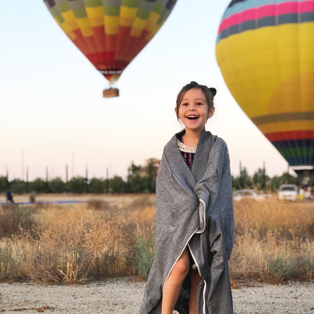 Fotografia de foco seletivo da menina coberta por lenço cinza com fundo de balões de ar quente