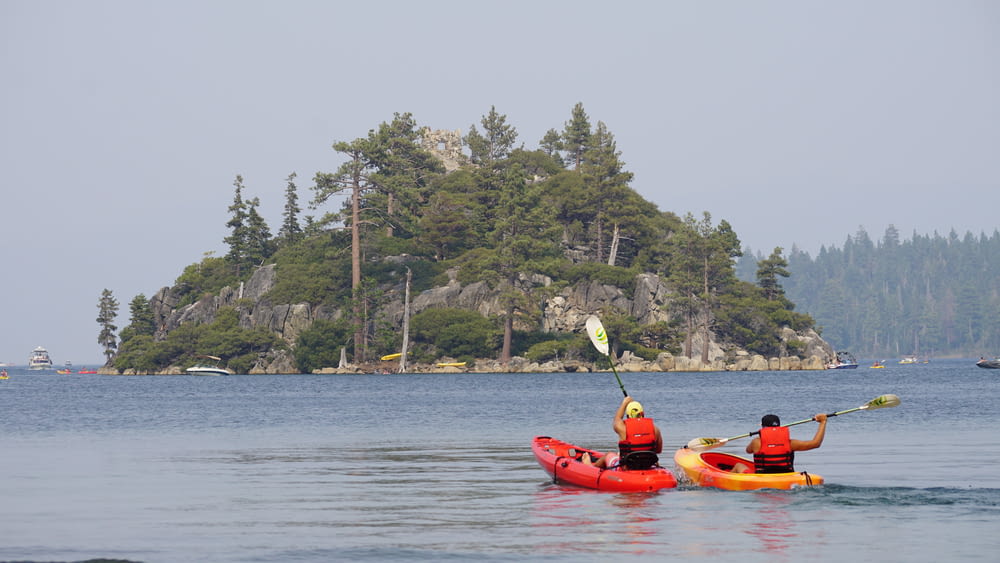 two person kayaking on water near islet