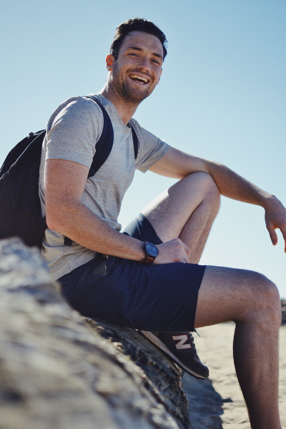 Uomo sorridente che si siede sulla roccia grigia durante il giorno