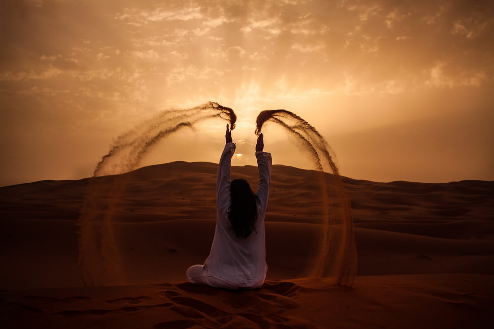 Mulher sentada no deserto enquanto joga areia durante a hora dourada