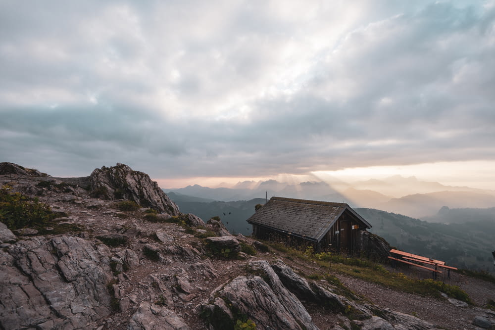 a cabin on a rocky mountain with a cloudy sky
