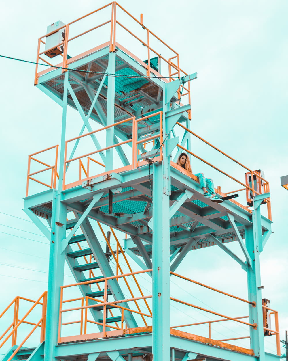 woman sitting on teal and yellow metal tower during daytime
