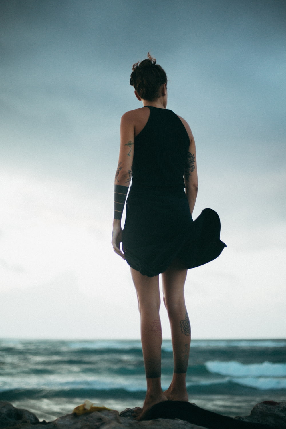 mulher em pé na rocha olhando para o mar durante o dia